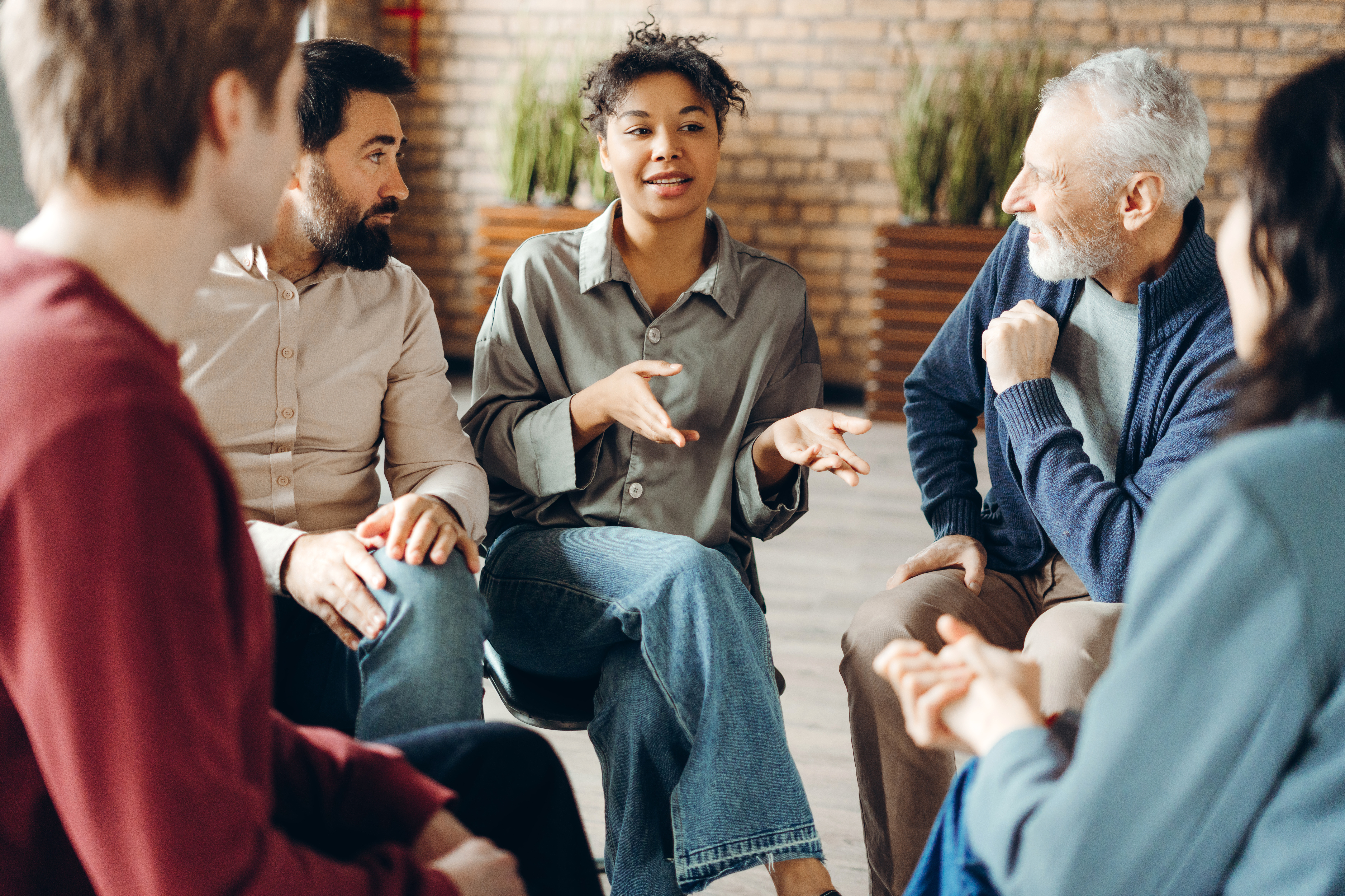 Diverse group of people sitting in a circle during a group therapy session, actively listening to a doctor who is facilitating the discussion