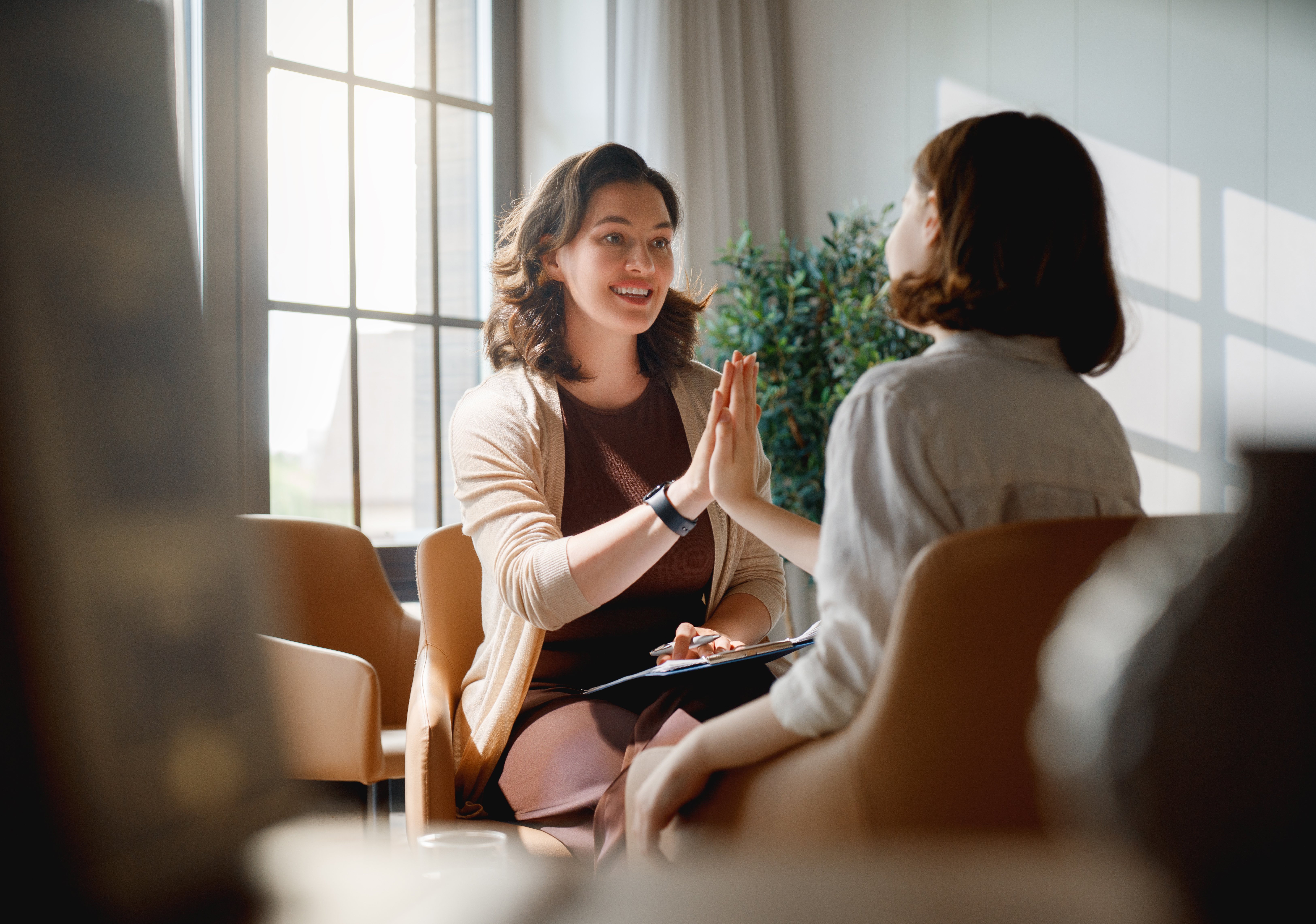 Heartwarming scene of a female therapist and a young client sharing an encouraging high five in a modern, sunlit office. The atmosphere conveys trust, growth, and emotional support, highlighting the value of positive connections and mental health care. Ideal for concepts of therapy, wellbeing, mentorship, counseling, psychological support, and professional guidance.